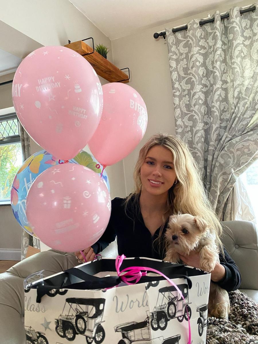 Aideen smiling with her small dog beside birthday balloons