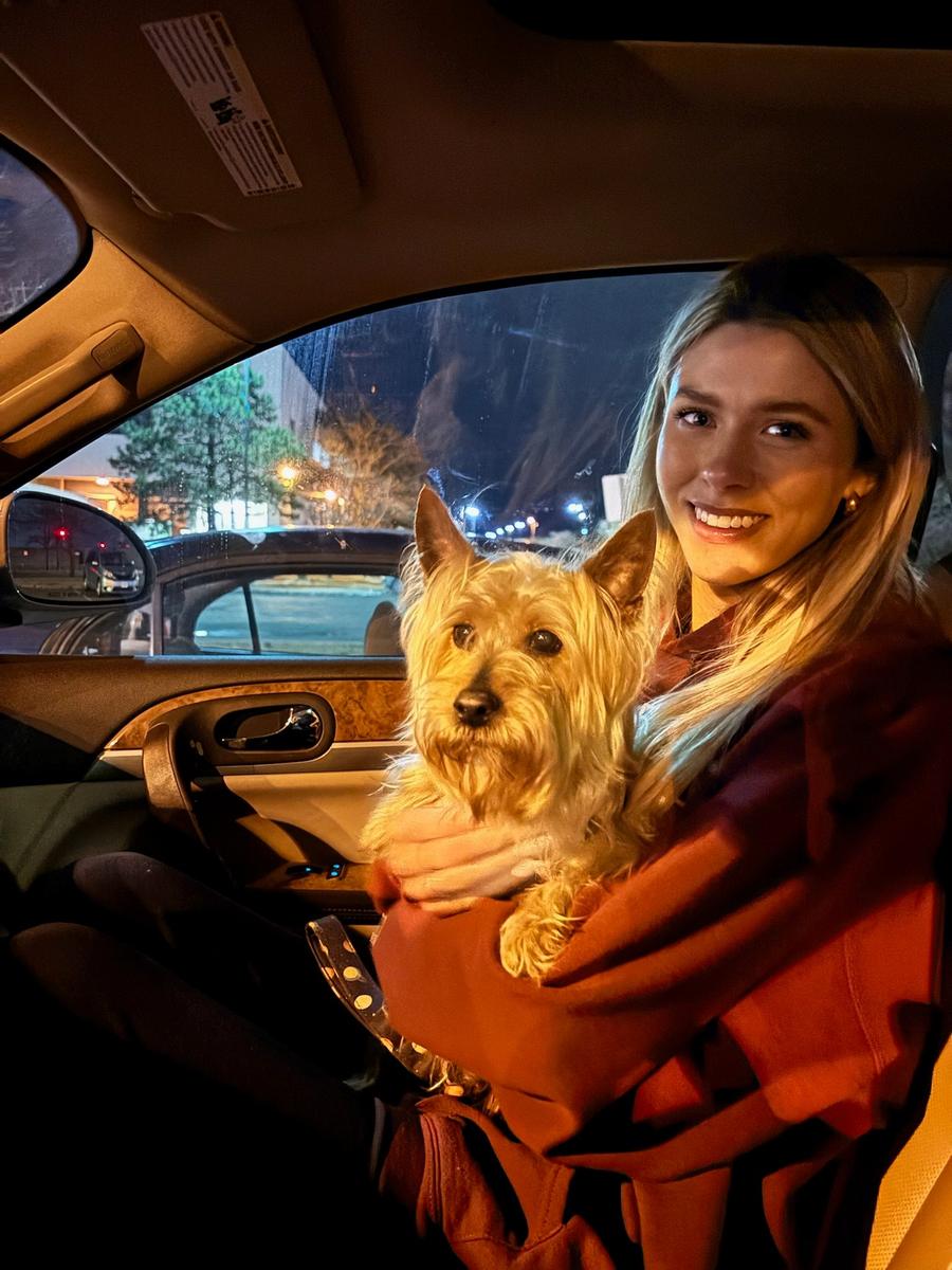 Aideen smiling with her small dog in a car at night