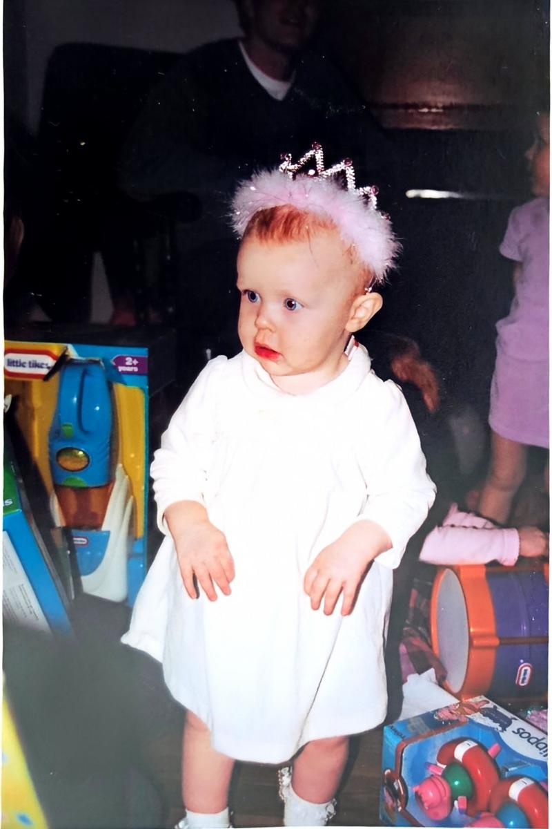 Aideen as a toddler wearing a toy tiara and white dress